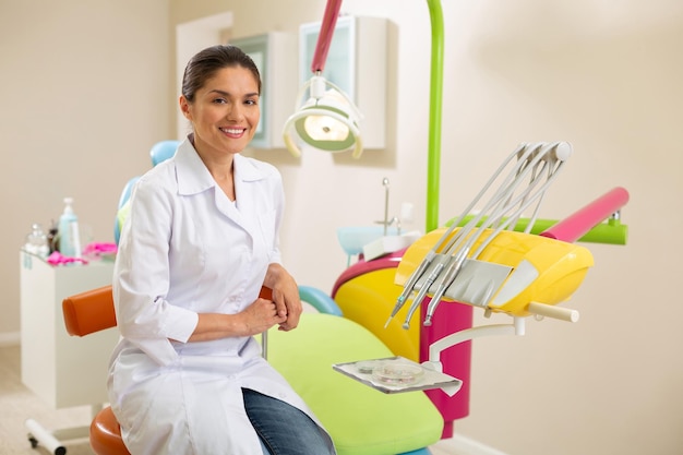 Smiling darkhaired female dentist sitting in her office