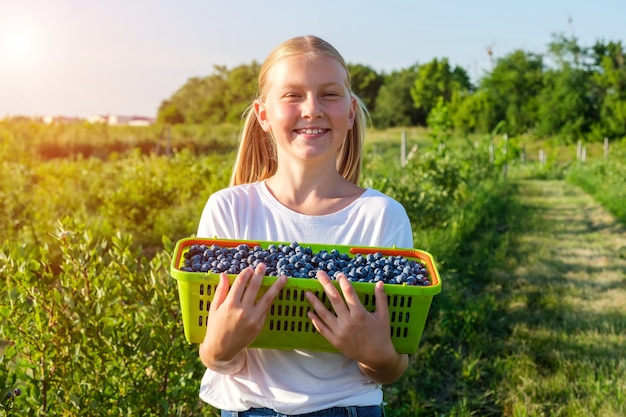 Smiling daughter of farmers harvests blueberries and holds a basket of berries