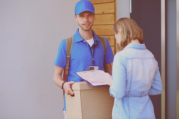 Smiling delivery man in blue uniform delivering parcel box to recipient courier service concept Smiling delivery man in blue uniform