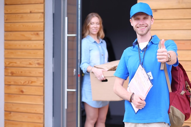 Smiling delivery man in blue uniform delivering parcel box to recipient courier service concept