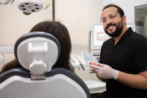 Smiling dentist with beard listens to female patient complains on toothache during appointment