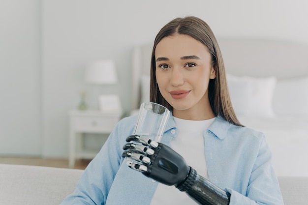 Smiling disabled girl holds glass with water by bionic prosthetic arm Disability healthy lifestyle