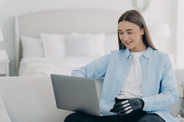 Smiling disabled girl student with bionic hand prosthesis working learning online at laptop at home