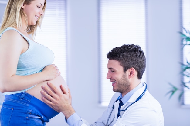 Smiling doctor checking stomach of standing pregnant patient