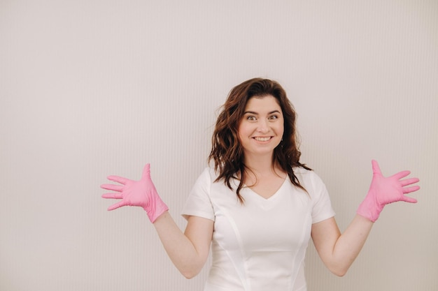 A smiling doctor in pink gloves and a white coat looks at the camera on a light background