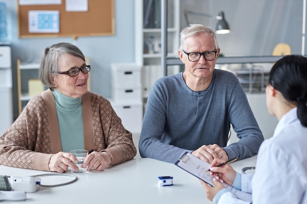 Smiling elderly couple consulting with doctor in clinic office