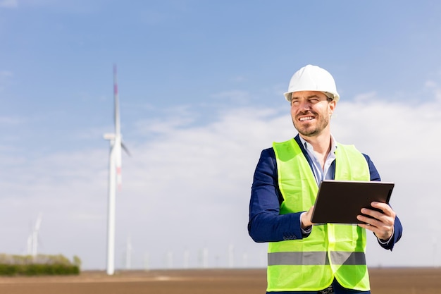 Smiling Engineer With Tablet Inspecting Wind Turbines On A Sunny Day