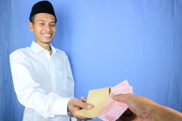 Smiling expression of Asian Muslim man giving money for helping donation or zakat