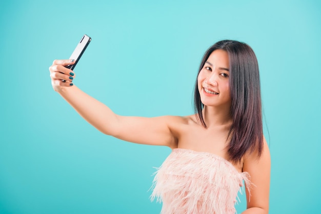 Smiling face portrait asian beautiful woman her standing making selfie photo on smartphone and her looking to camera on blue background