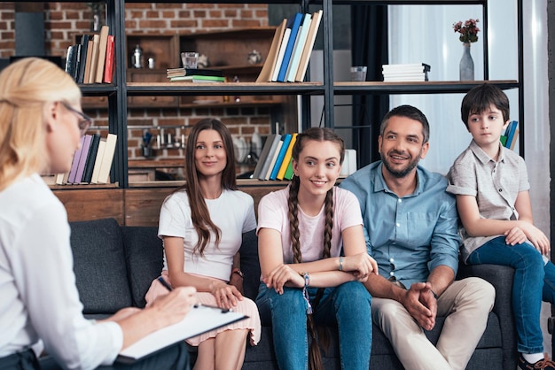 Smiling family on therapy session by female counselor writing in clipboard in office