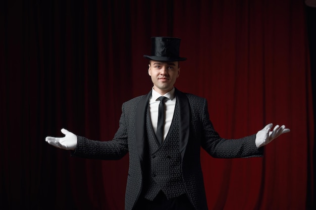 Smiling fashionable showman or illusionist in tailcoat and top hat on stage