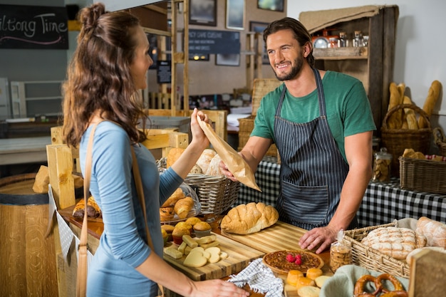 Smiling female customer receiving a parcel from bakery staff at counter