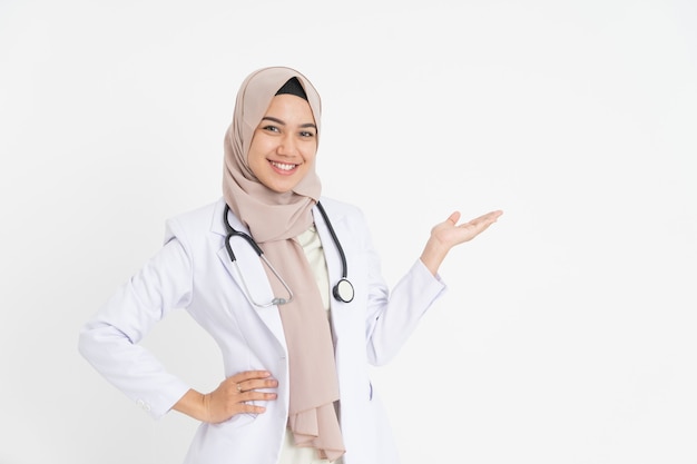 Smiling female doctor in headscarf with offering gesture looking at the camera with space