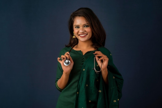 A smiling female doctor wearing a stethoscope on her shoulders looking at the camera on gray background