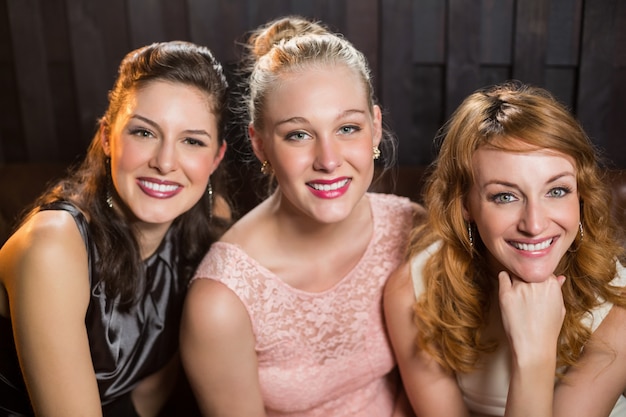 Smiling female friends sitting together in sofa at bar