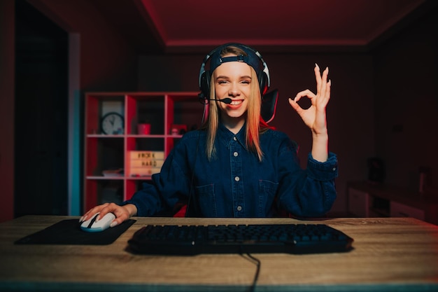 Smiling female gamer in casual clothes and headset on her head sitting at home at the computer