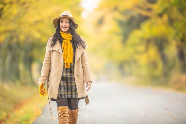 Smiling female having an autumn walk outdoors surrounded by yellow trees.