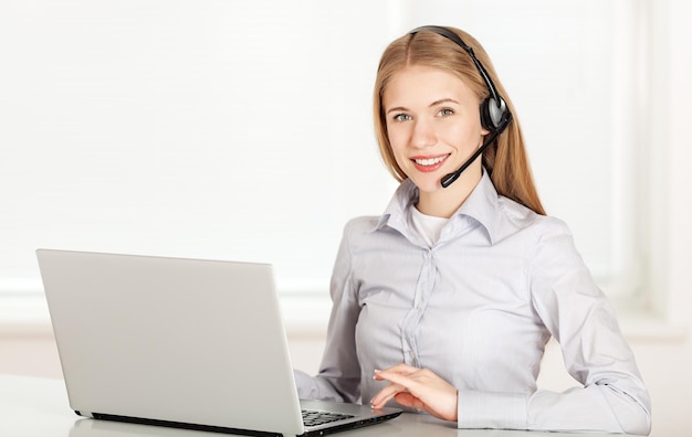 smiling female helpline operator with headphones and laptop