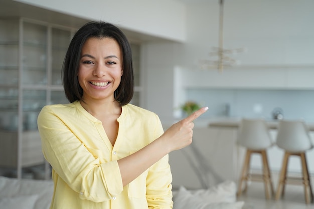 Smiling female homeowner pointing aside recommending service real estate sale offer at new home