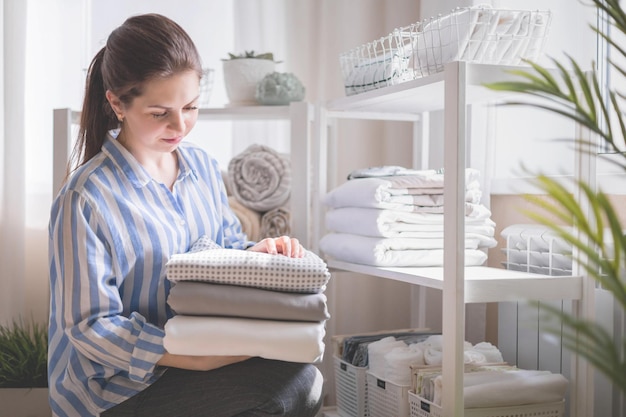 Photo smiling female in pajamas enjoying homework bedroom minimalist cupboard storage space organizing happy housewife making seasonal tidying up putting folded linens use marie kondo method at home