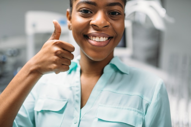 Smiling female patient shows thumbs up in dental clinic