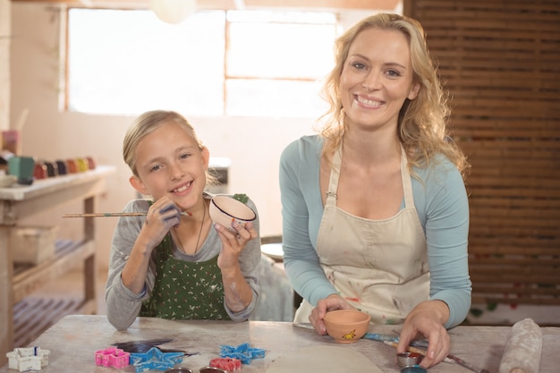 Smiling female potter and girl painting in pottery workshop