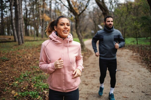 Smiling fit woman running fast in front of her friend. They are exercising for marathon.