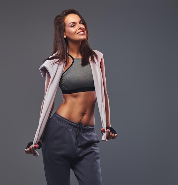 Smiling fitness brunette female in a gray sportswear posing in a studio. Isolated on a gray background.