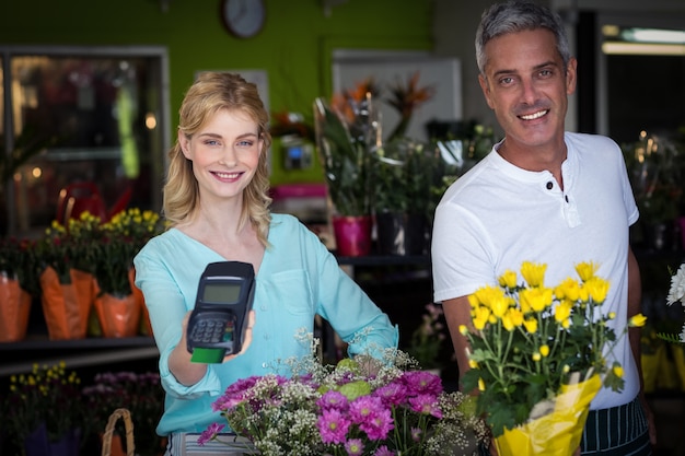 Smiling florist showing credit card terminal in flower shop