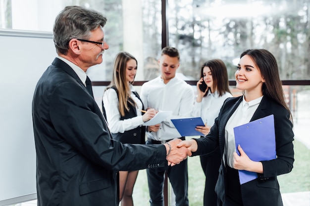 Smiling friendly  older businessman shaking hands with woman stay at  office.