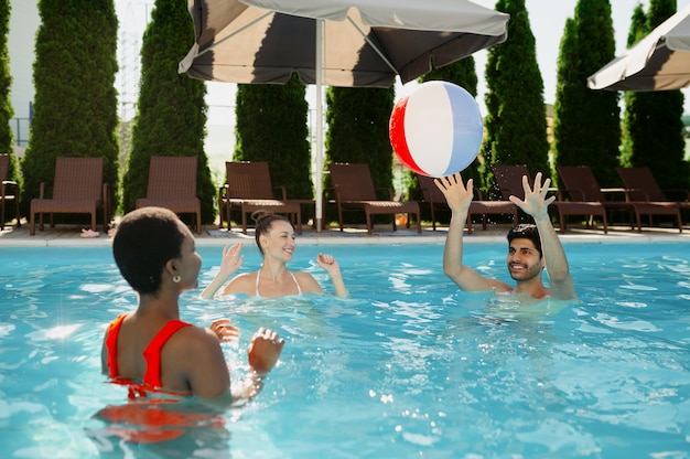 Smiling friends play with ball in the pool