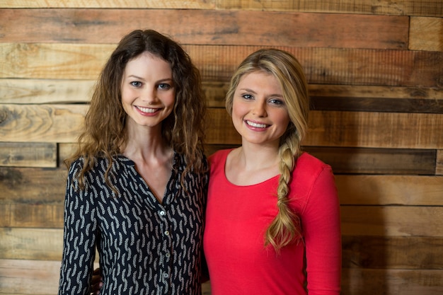 Smiling friends standing against wooden wall in coffee