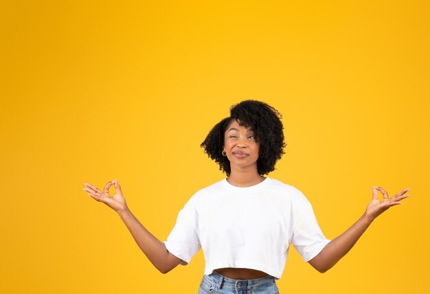 Smiling funny young african american curly lady in white tshirt meditating look with one eye at