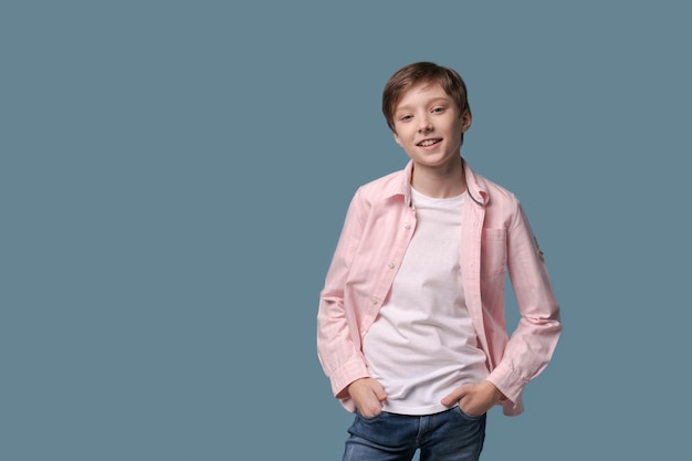 Smiling funny young man in casual white tshirt and pink shirt posing on light