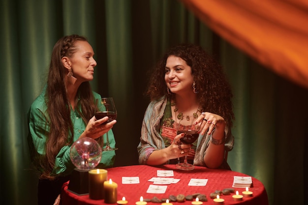 Smiling future tellers drinking wine and spreading tarot cards