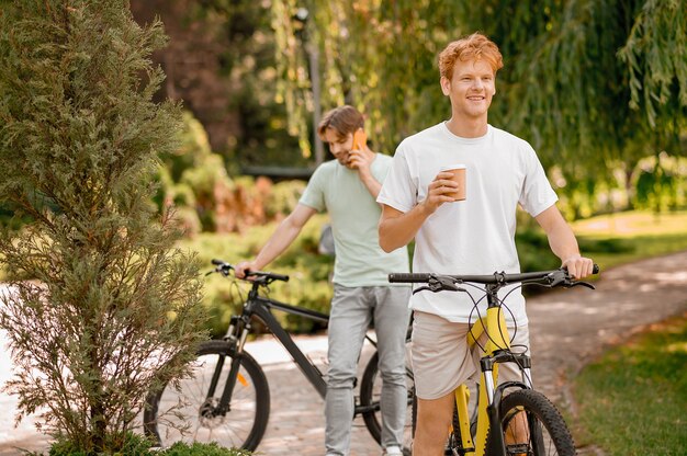 Smiling ginger man with a disposable paper cup and his dark-haired pal with a smartphone