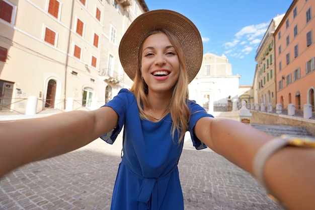 Smiling girl in blue dress and hat takes selfie picture in Ancona Marche Italy