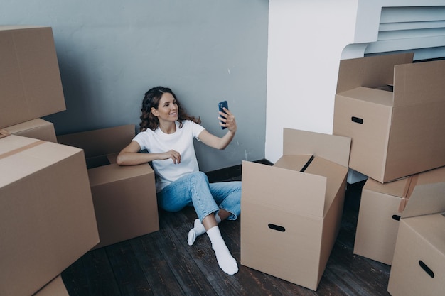 Smiling girl chatting by video call discussing relocation details holding smartphone on moving day