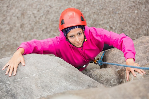 Smiling girl climbing up rock face 