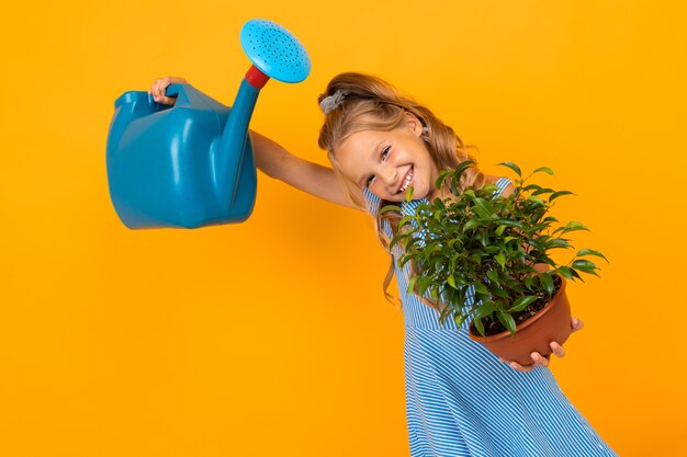 Photo smiling girl in a dress holds a plant and a watering can on an orange wall