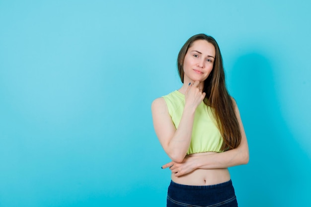 Smiling girl is looking at camera by putting hand under chin on blue background