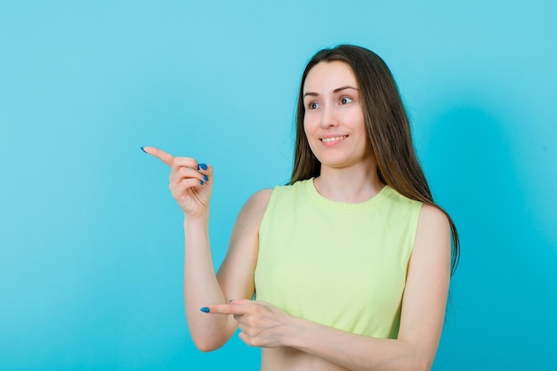 Smiling girl is pointing right away with forefinger on blue background