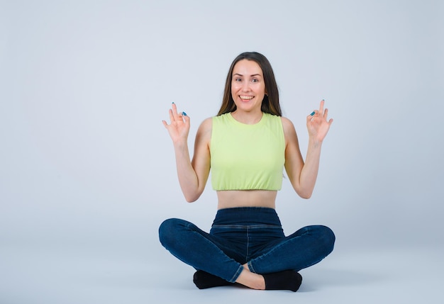 Smiling girl is showing okay gestures by sitting on floor on white background