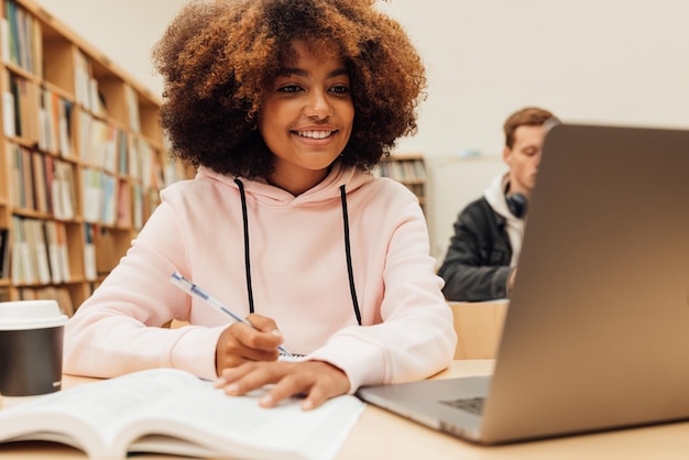 Smiling girl looking at laptop while studying in library