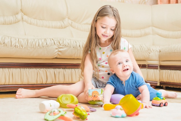 Smiling girl playing with her sibling baby on carpet