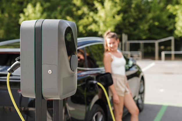 Photo smiling girl plugging cable charger into her black electric car and connecting it with ev charging