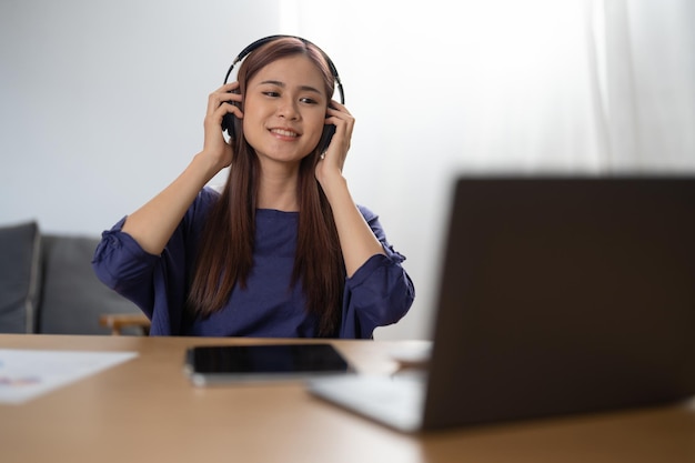 Smiling girl relaxing at home she is playing music using a laptop and wearing headphones