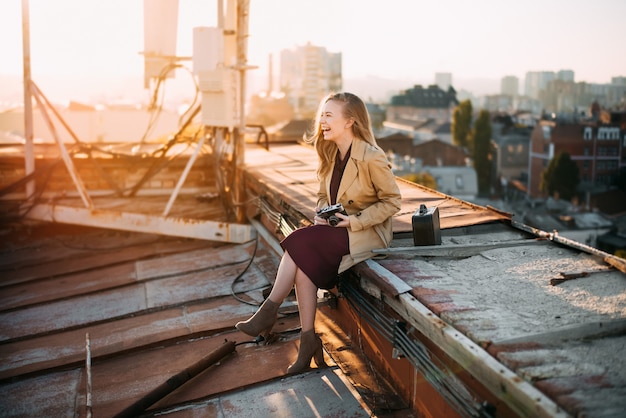 Smiling girl on the roof with camera Young blonde posing at sunset