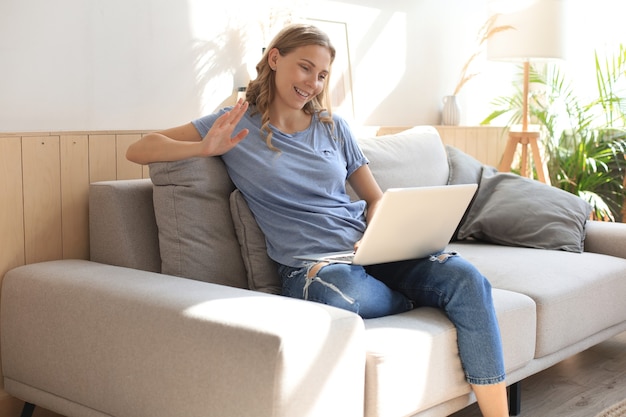 Smiling girl sit on couch watching webinar on laptop. Happy young woman study on online distant course.