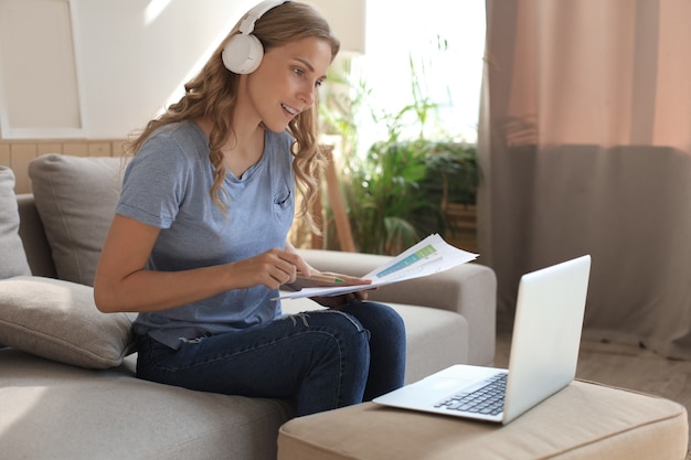 Smiling girl sit near couch watching webinar on laptop. Happy young woman study on online distant course.